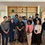 Diverse group of coworkers posing together for a photo in an office lobby. Everyone is smiling.