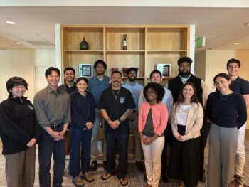 Diverse group of coworkers posing together for a photo in an office lobby. Everyone is smiling.